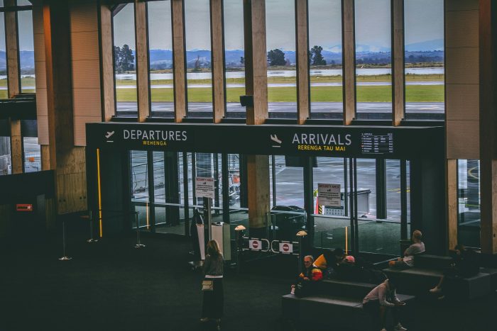 Busy airport terminal area with people, featuring departures and arrivals signs.