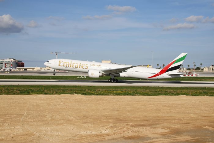 Emirates Boeing 777 aircraft on runway under clear blue sky.